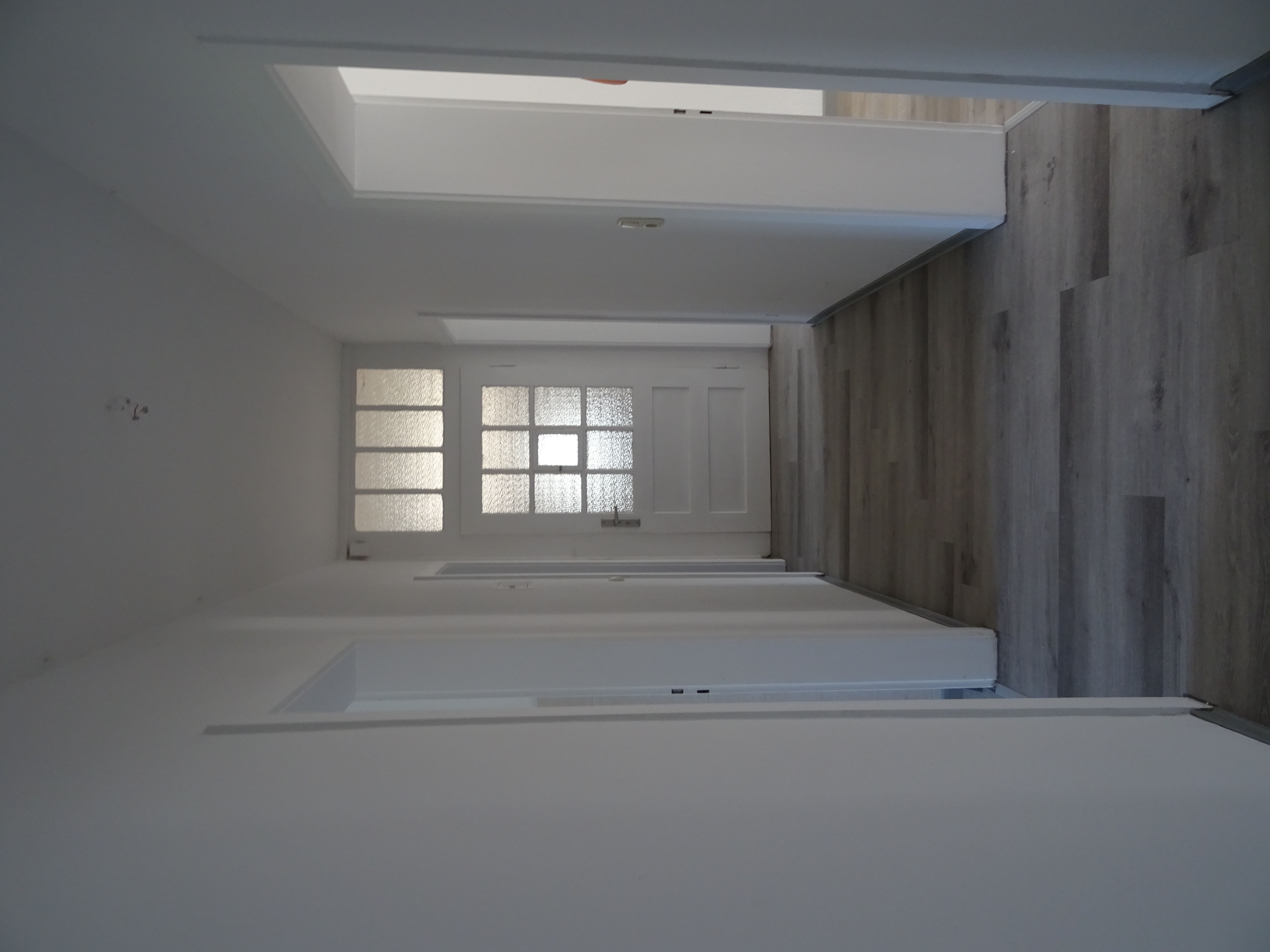 Foto eines sanierten Flurs, graues Laminat, weiß gestrichene Wände, weiße Haustür